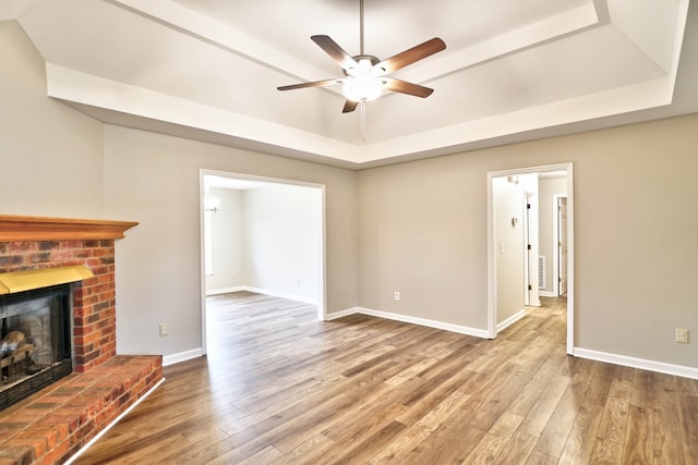 unfurnished living room featuring a tray ceiling, a fireplace, ceiling fan, and hardwood / wood-style floors