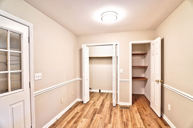 unfurnished bedroom with light wood-type flooring and multiple closets