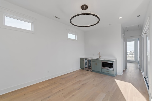 bar with sink, stainless steel microwave, beverage cooler, and light hardwood / wood-style flooring