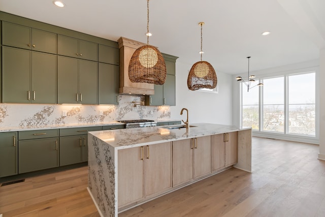 kitchen with light stone counters, sink, an island with sink, and light hardwood / wood-style flooring