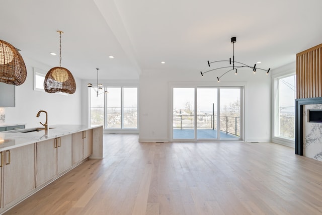 kitchen with an inviting chandelier, light stone counters, light hardwood / wood-style flooring, pendant lighting, and light brown cabinetry