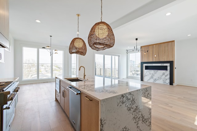 kitchen featuring sink, stainless steel appliances, light stone counters, light hardwood / wood-style floors, and a center island with sink