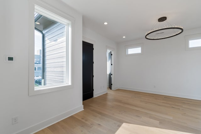 unfurnished room with an inviting chandelier, a healthy amount of sunlight, and light wood-type flooring