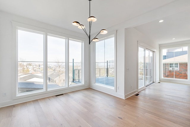 unfurnished dining area featuring a chandelier, light hardwood / wood-style floors, and a wealth of natural light