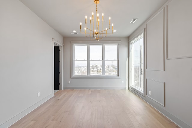 unfurnished dining area featuring a chandelier, a healthy amount of sunlight, and light hardwood / wood-style floors