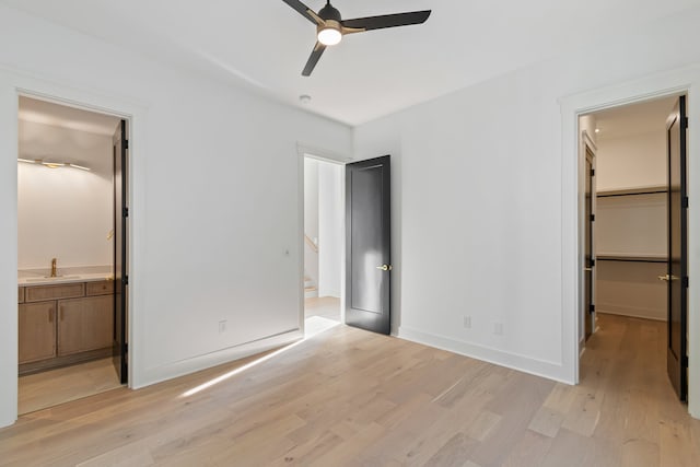 unfurnished bedroom with light wood-type flooring, a spacious closet, ensuite bath, and ceiling fan