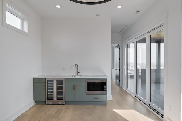 bar featuring light wood-type flooring, sink, green cabinetry, wine cooler, and stainless steel microwave