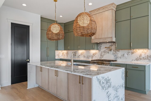 kitchen featuring light hardwood / wood-style flooring, an island with sink, green cabinetry, and sink