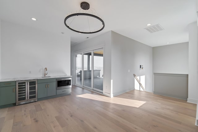 bar with wine cooler, stainless steel microwave, light hardwood / wood-style floors, and sink