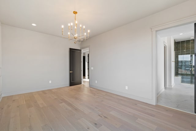 spare room featuring light wood-type flooring and a chandelier