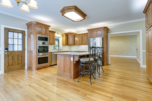 kitchen featuring crown molding, light wood-type flooring, decorative light fixtures, a kitchen island, and stainless steel appliances