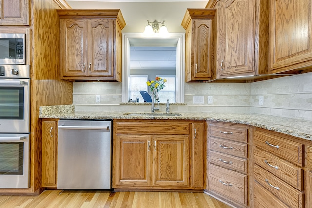 kitchen featuring light stone counters, sink, light wood-type flooring, and appliances with stainless steel finishes