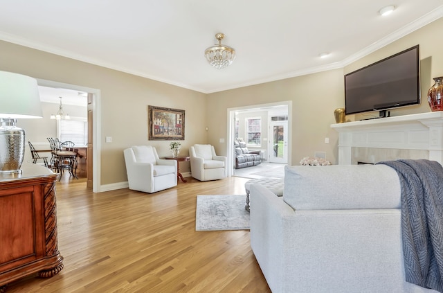 living room featuring crown molding, a fireplace, an inviting chandelier, and light wood-type flooring