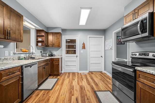 kitchen with light stone counters, sink, stainless steel appliances, and light hardwood / wood-style floors