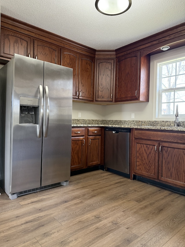 kitchen with light hardwood / wood-style floors, light stone counters, a textured ceiling, and appliances with stainless steel finishes