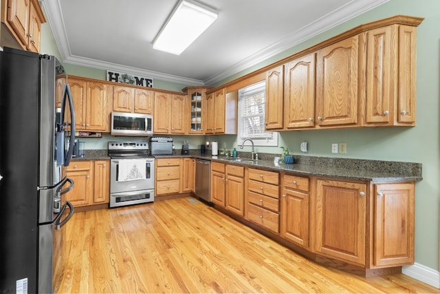 kitchen with sink, light hardwood / wood-style flooring, dark stone countertops, appliances with stainless steel finishes, and ornamental molding