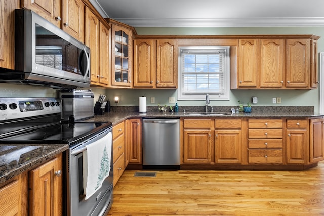 kitchen featuring sink, light hardwood / wood-style flooring, dark stone countertops, crown molding, and appliances with stainless steel finishes