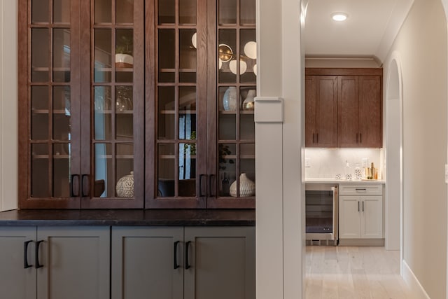 bar featuring light wood-type flooring, crown molding, and wine cooler