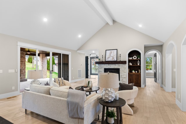 living room featuring a stone fireplace, beamed ceiling, high vaulted ceiling, and light hardwood / wood-style floors