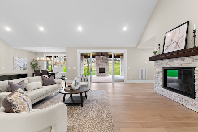 living room featuring light wood-type flooring, an inviting chandelier, a stone fireplace, and high vaulted ceiling