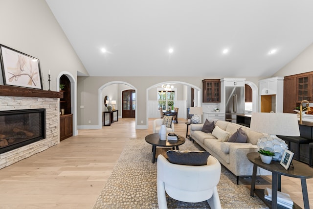 living room featuring sink, light hardwood / wood-style flooring, high vaulted ceiling, a notable chandelier, and a fireplace