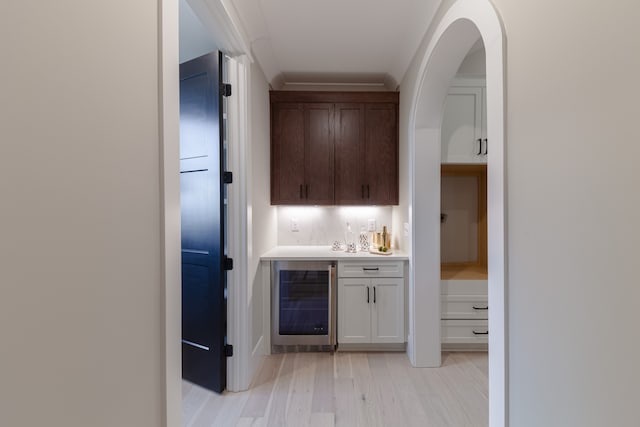 bar featuring wine cooler, light hardwood / wood-style flooring, white cabinets, and dark brown cabinets