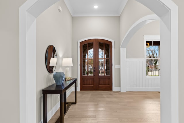 foyer with a healthy amount of sunlight, light wood-type flooring, crown molding, and french doors