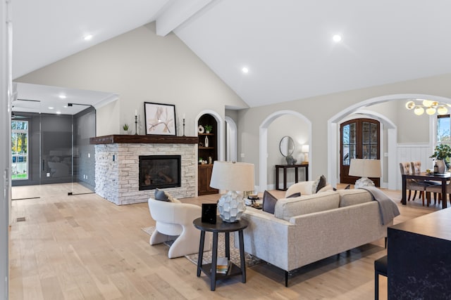 living room with a fireplace, high vaulted ceiling, a healthy amount of sunlight, and light wood-type flooring