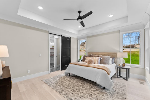 bedroom featuring a tray ceiling, a barn door, ceiling fan, and light hardwood / wood-style flooring