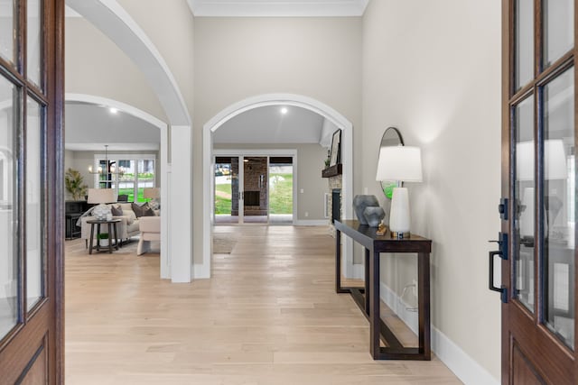 foyer with a stone fireplace, light wood-type flooring, a high ceiling, and a chandelier