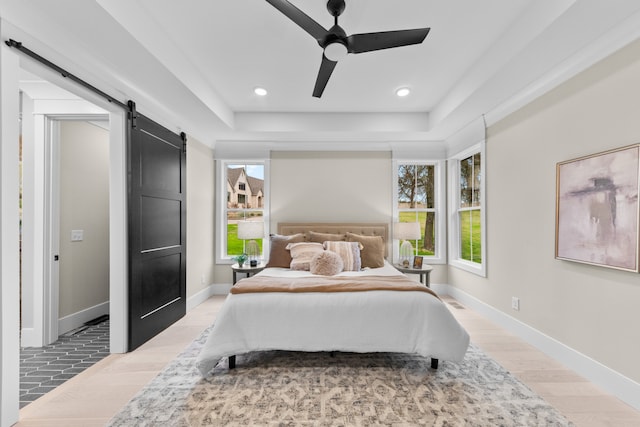 bedroom featuring a barn door, ceiling fan, and light hardwood / wood-style floors