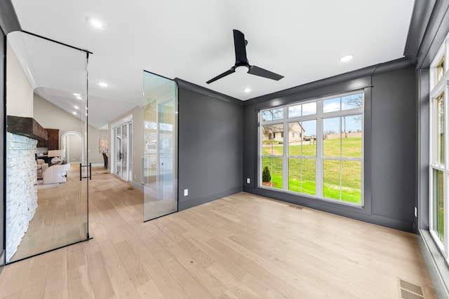 unfurnished room featuring light hardwood / wood-style floors, a stone fireplace, ceiling fan, and a healthy amount of sunlight