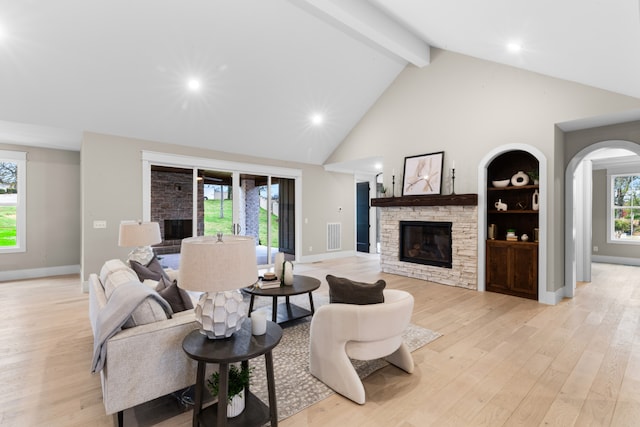 living room featuring beamed ceiling, high vaulted ceiling, light hardwood / wood-style floors, and a stone fireplace