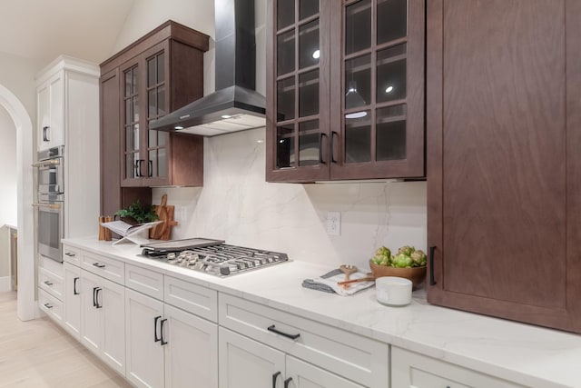 kitchen with backsplash, wall chimney range hood, light stone countertops, appliances with stainless steel finishes, and white cabinetry