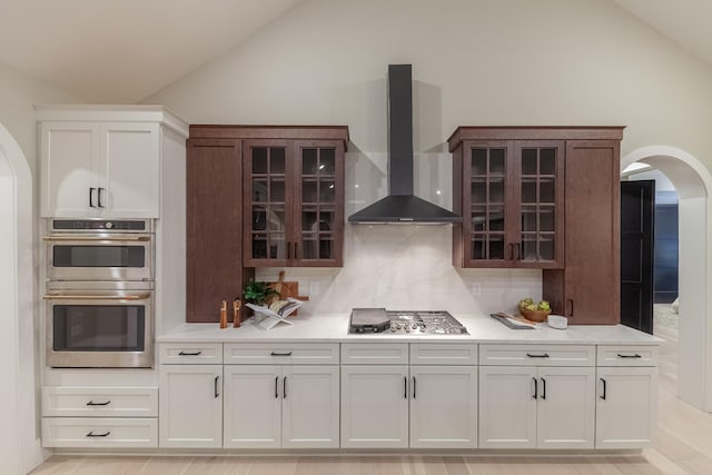 kitchen with vaulted ceiling, wall chimney exhaust hood, appliances with stainless steel finishes, tasteful backsplash, and white cabinetry