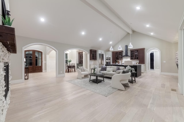 living room with beamed ceiling, light hardwood / wood-style floors, high vaulted ceiling, and a stone fireplace