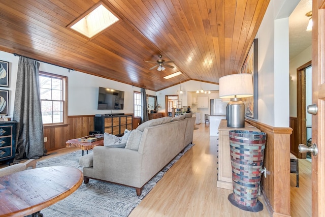 living room featuring wood ceiling, lofted ceiling with skylight, ceiling fan, light hardwood / wood-style flooring, and wood walls