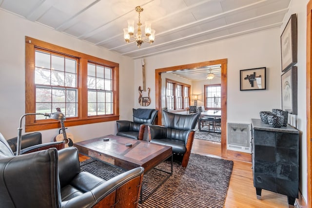 living room with beamed ceiling, a healthy amount of sunlight, ceiling fan with notable chandelier, and light wood-type flooring