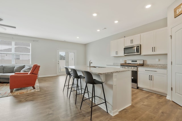 kitchen with appliances with stainless steel finishes, a center island with sink, white cabinetry, and light hardwood / wood-style floors