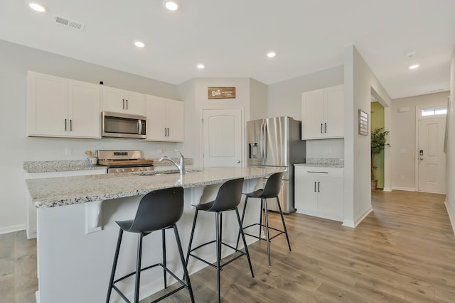 kitchen featuring light stone countertops, appliances with stainless steel finishes, light wood-type flooring, white cabinetry, and an island with sink