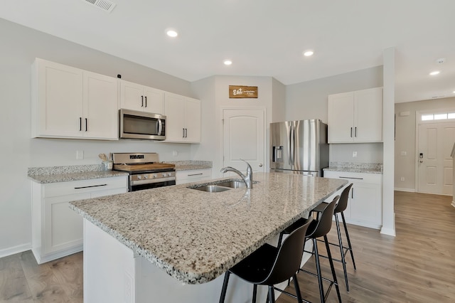 kitchen with a center island with sink, sink, light hardwood / wood-style flooring, appliances with stainless steel finishes, and white cabinetry