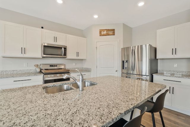 kitchen with light stone countertops, appliances with stainless steel finishes, white cabinetry, and dark wood-type flooring