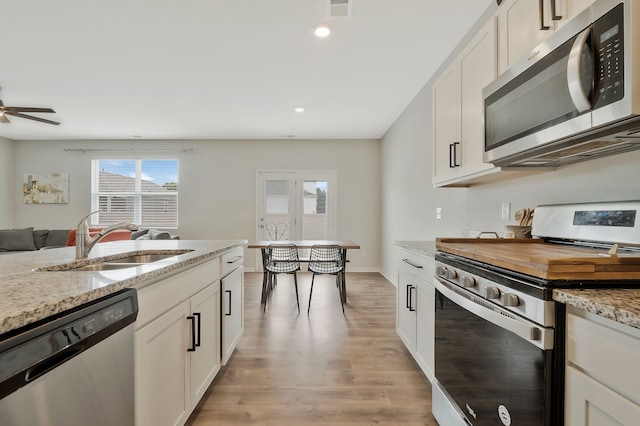 kitchen featuring sink, light hardwood / wood-style flooring, appliances with stainless steel finishes, light stone counters, and white cabinetry