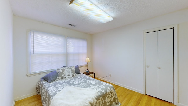 bedroom with a closet, a textured ceiling, and light wood-type flooring