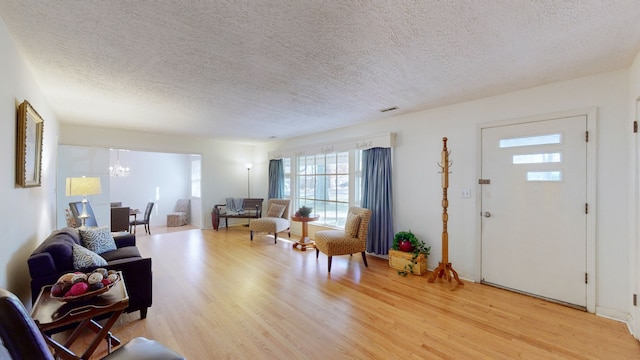 living room featuring a notable chandelier, light wood-type flooring, and a textured ceiling