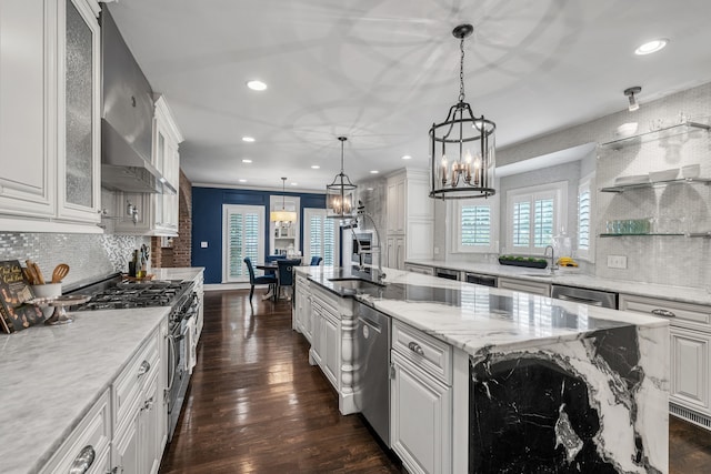 kitchen with appliances with stainless steel finishes, pendant lighting, white cabinetry, a kitchen island with sink, and light stone countertops