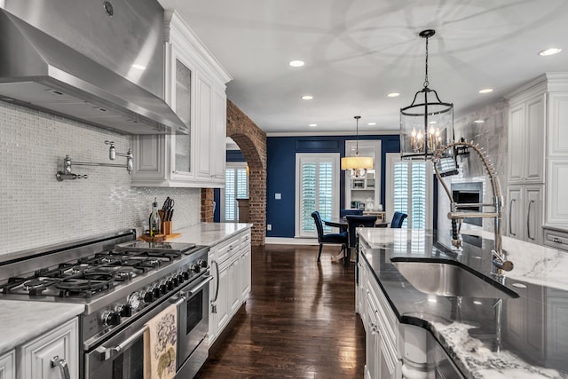 kitchen with pendant lighting, white cabinetry, double oven range, light stone countertops, and wall chimney range hood