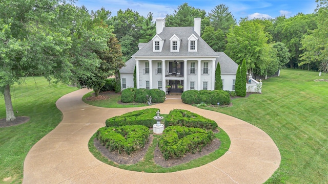 view of front of home featuring a chimney, covered porch, a shingled roof, and a front lawn