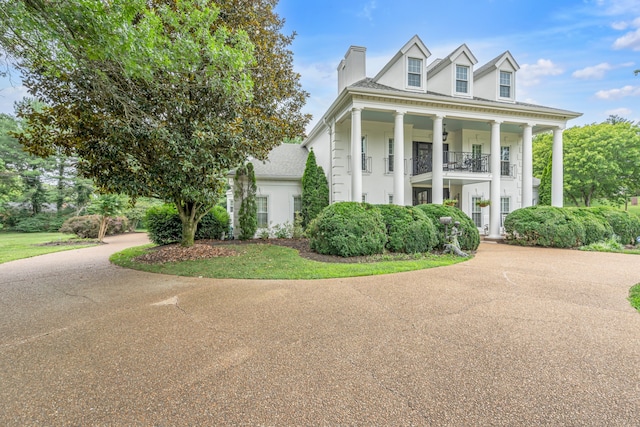 neoclassical / greek revival house featuring concrete driveway, a balcony, and a chimney