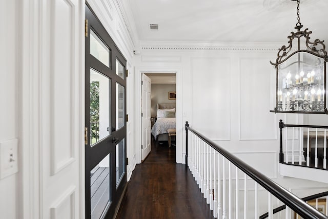 corridor featuring visible vents, a chandelier, ornamental molding, dark wood-style floors, and a decorative wall